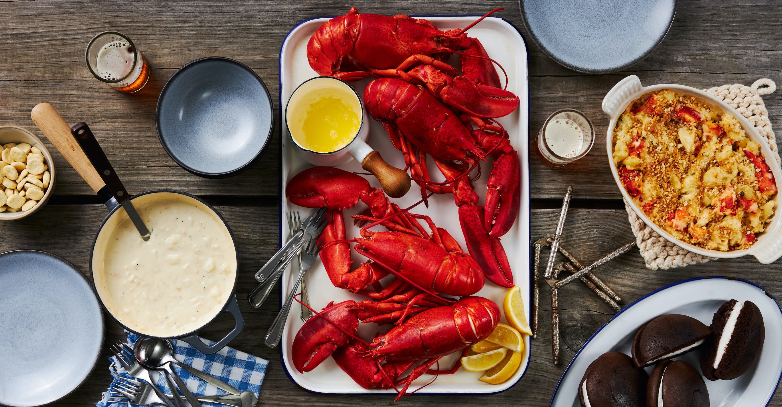 An overhead shot of our Vacationland Family Meal, with 4 steamed lobster, lobster mac & cheese, chocolate whoopie pies, and clam chowder, surrounded by table settings.